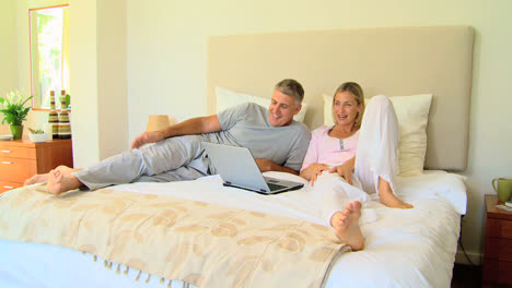 attractive couple relaxing on bed with laptop