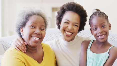portrait of smiling african american mother, daughter and grandmother embracing at home, slow motion