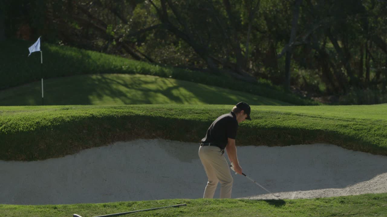 골퍼가 골프 코스의 모래 함정에서 스윙을 합니다.