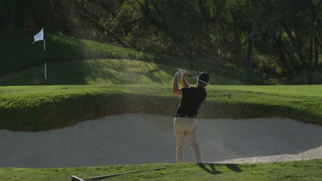 un golfista hace un swing en una trampa de arena en un campo de golf