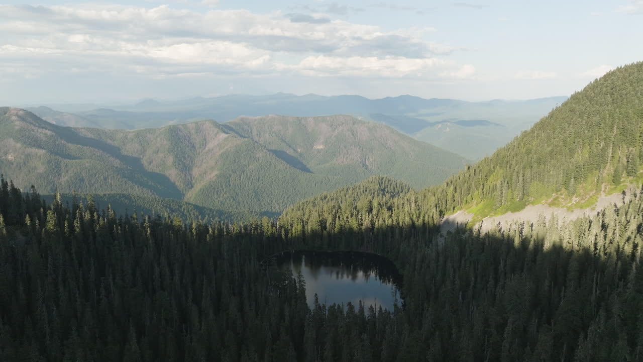 Very slow flyover above small alpine lake in Gifford Pinchot National Forest, aerial establishing view, nature background.