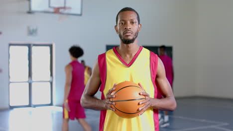 hombre afroamericano sostiene una pelota de baloncesto en un gimnasio
