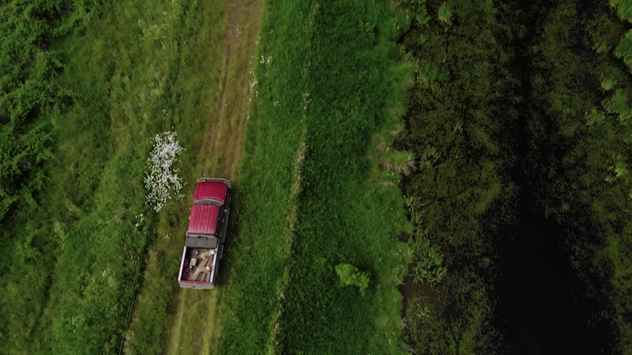 그린필드로 둘러싸인 거친 도로를 여행하는 빨간 트럭의 조감도