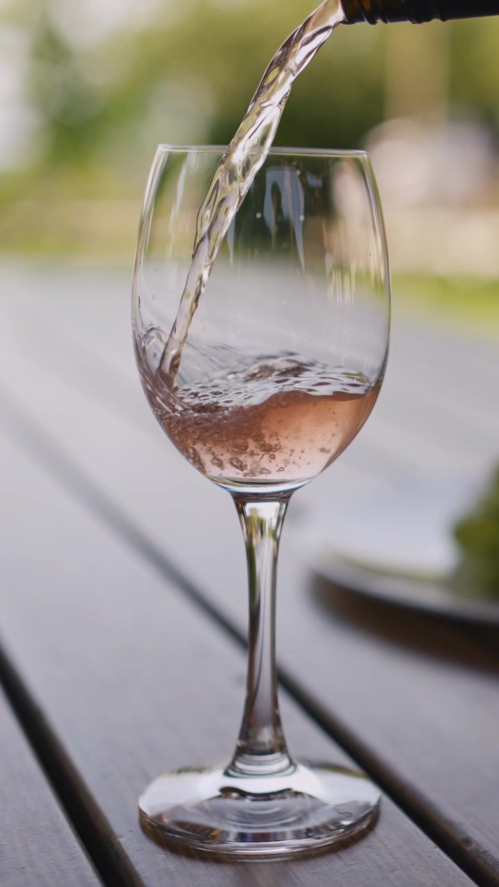 Lodret video nærbillede af rosévin, der hældes i et klart glas på et træbord udendørs. Blødt dagslys, skarpt fokus – ideel til sociale medier.
