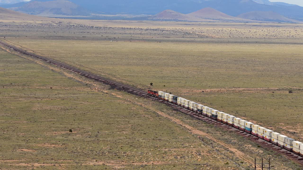 A drone following shot tracks freight train as the drone moves to reveal a vast southwest landscape, illustrating the intersection of industry and nature