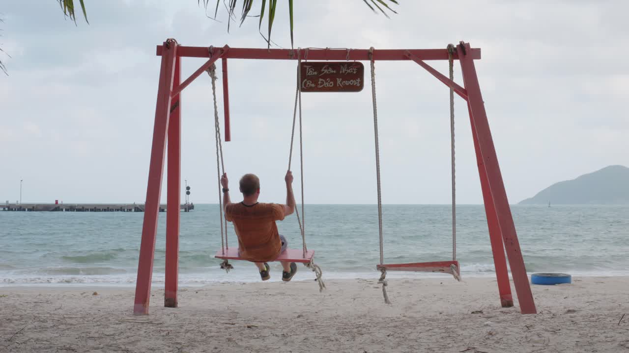 hombre disfrutando del columpio en la playa mientras mira al océano