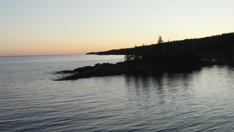 aerial view flying away from lake superior shoreline at sunset revealing dikes and forested landscape - drone flying shot