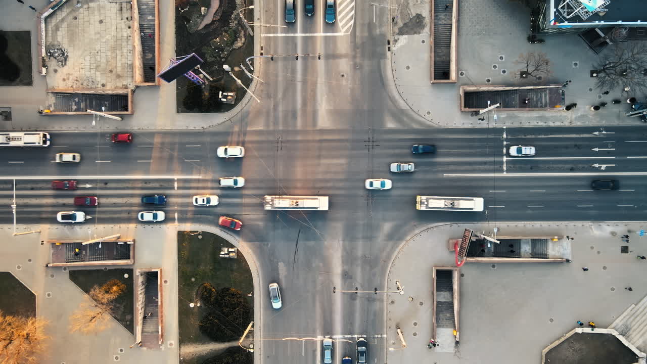 Aerial drone view of intersection at sunset. Road with multiple cars, walking people, underground passage. Bare trees, winter