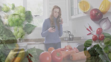 animation of vegetables and fruit over caucasian woman using smartphone and drinking coffee