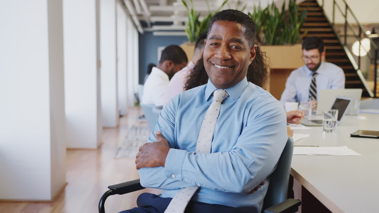 retrato de un hombre de negocios maduro en una oficina moderna con colegas reunidos alrededor de una mesa en el fondo