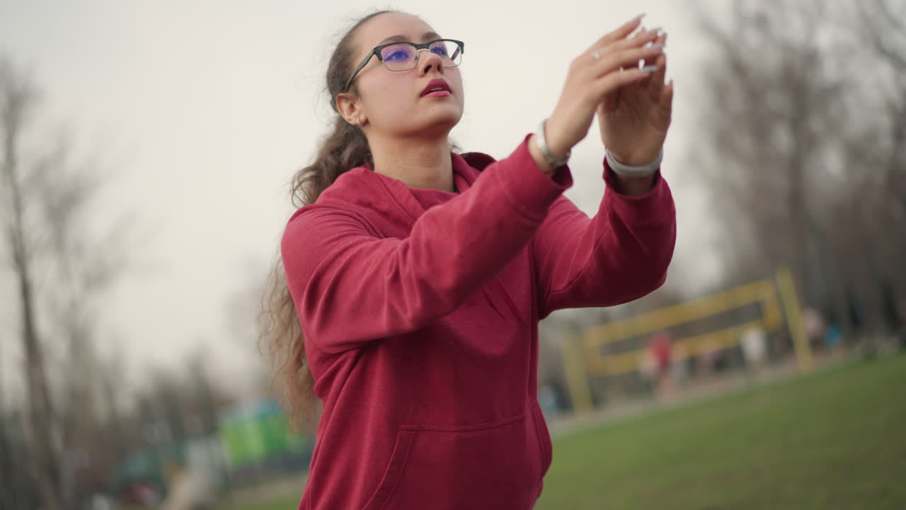 Young Woman Performing Stance Demonstration, Female Demonstrating Hip Flexibility Outdoors, Young Female Athlete Showcasing Hip Range And Stance Amidst Park Environment With Nearby Playground