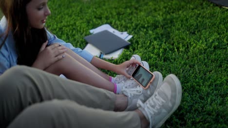 young couple sitting on the grass, looking at a phone