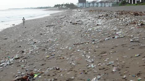 tracking shot of a man jogging on a badly polluted beach, tons of plastic garbage on the shore