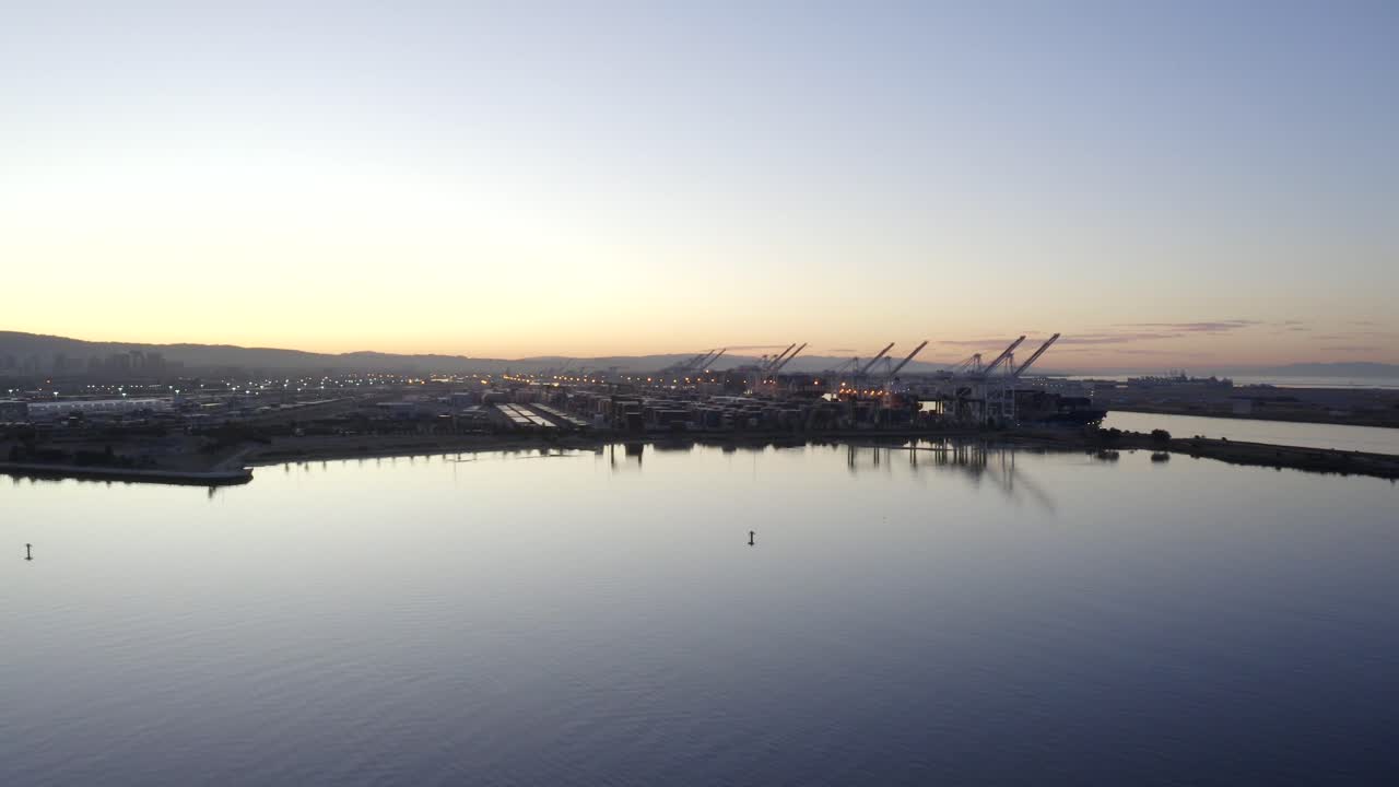 Nice long pan to the left past large industrial shipping cranes and the port. Sunrise in the morning with a rush of color and depth.