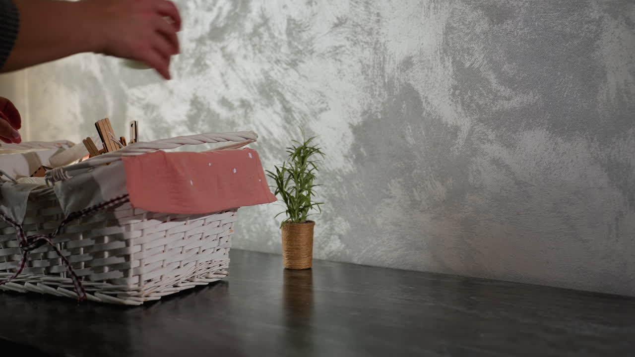 Close up of young adult in plaid clothing dropping white basket filled with various items onto dark marble kitchen table and starting to remove contents