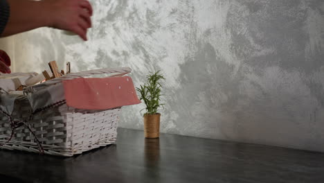close up of young adult in plaid clothing dropping white basket filled with various items onto dark marble kitchen table and starting to remove contents