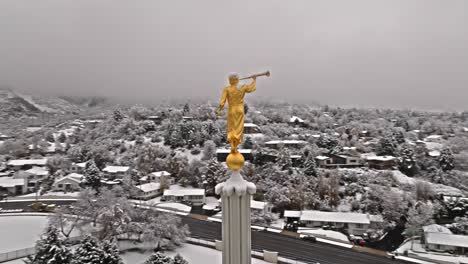 drone circles around golden angel with trumpet with snow covered neighborhood behind