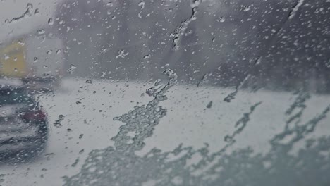 Close-up-view-of-a-snowflake-falling-on-the-windshield-of-the-car,-and-they-slide-down-the-glass-surface