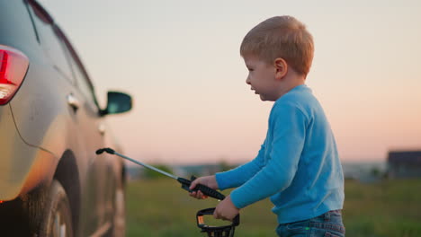 little kid sprays water on parents car in field cute little boy in blue sweater cleans automobile