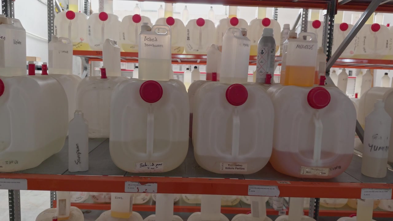 Múltiples garrafas grandes de plástico con tapas rojas que contienen líquidos químicos, apiladas en robustas estanterías de almacén industrial