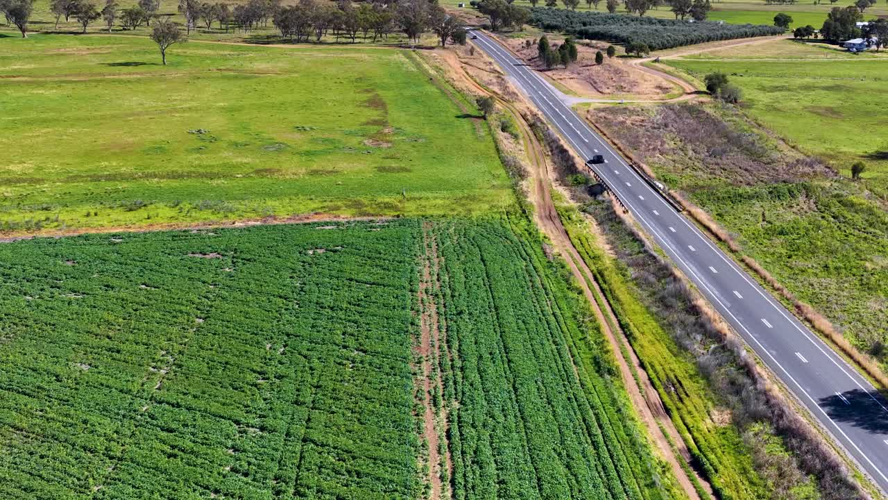 Drone footage captures a smooth aerial flyover above a rural road and green farmland near Armidale, New South Wales, under bright daylight with clear skies