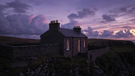 warm light spilling from the window of a stone cottage on a cliff overlooks the ocean at sunset, with vibrant purple and pink hues painting the sky and dramatic clouds enhancing the tranquil scene