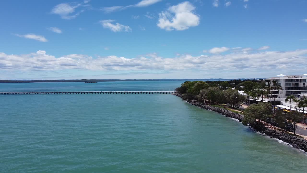 매우 긴 부두와 해변 마을을 보여주는 바다로 날아가는 드론