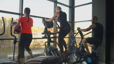 young fit woman using an elliptic trainer in a fitness center. a group of young women train on sports training equipment in a fitness gym. steady cam shot.