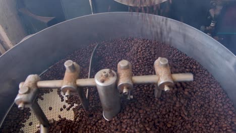 Freshly-roasted-and-golden-brown-Arabica-coffee-beans-spilling-from-industrial-coffee-roaster-machine-into-cooling-tray-during-roasting-process