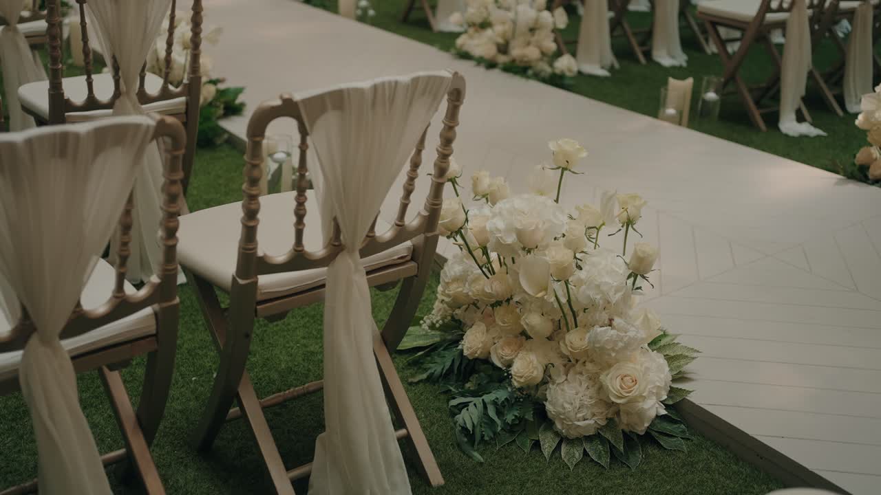 Fiori bianchi e sedie drappeggiate costeggiano un elegante corridoio nuziale all'aperto