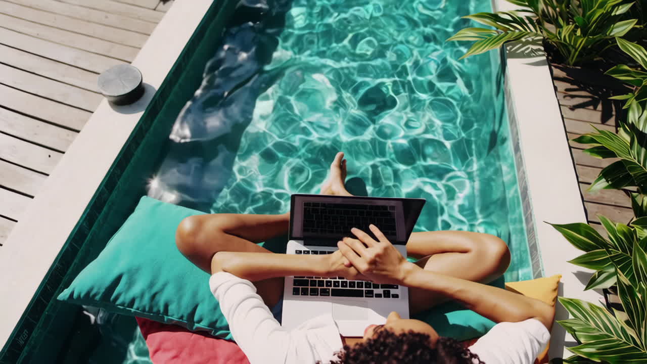 Woman working on laptop by a swimming pool