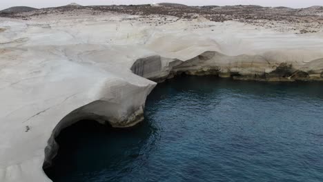 Vista-De-Drones-En-Grecia-Volando-Sobre-Un-área-De-Roca-Blanca-En-Forma-De-Luna-En-Arco-Recto-En-La-Isla-De-Milos-Al-Amanecer-Junto-Al-Mar-Azul-Oscuro