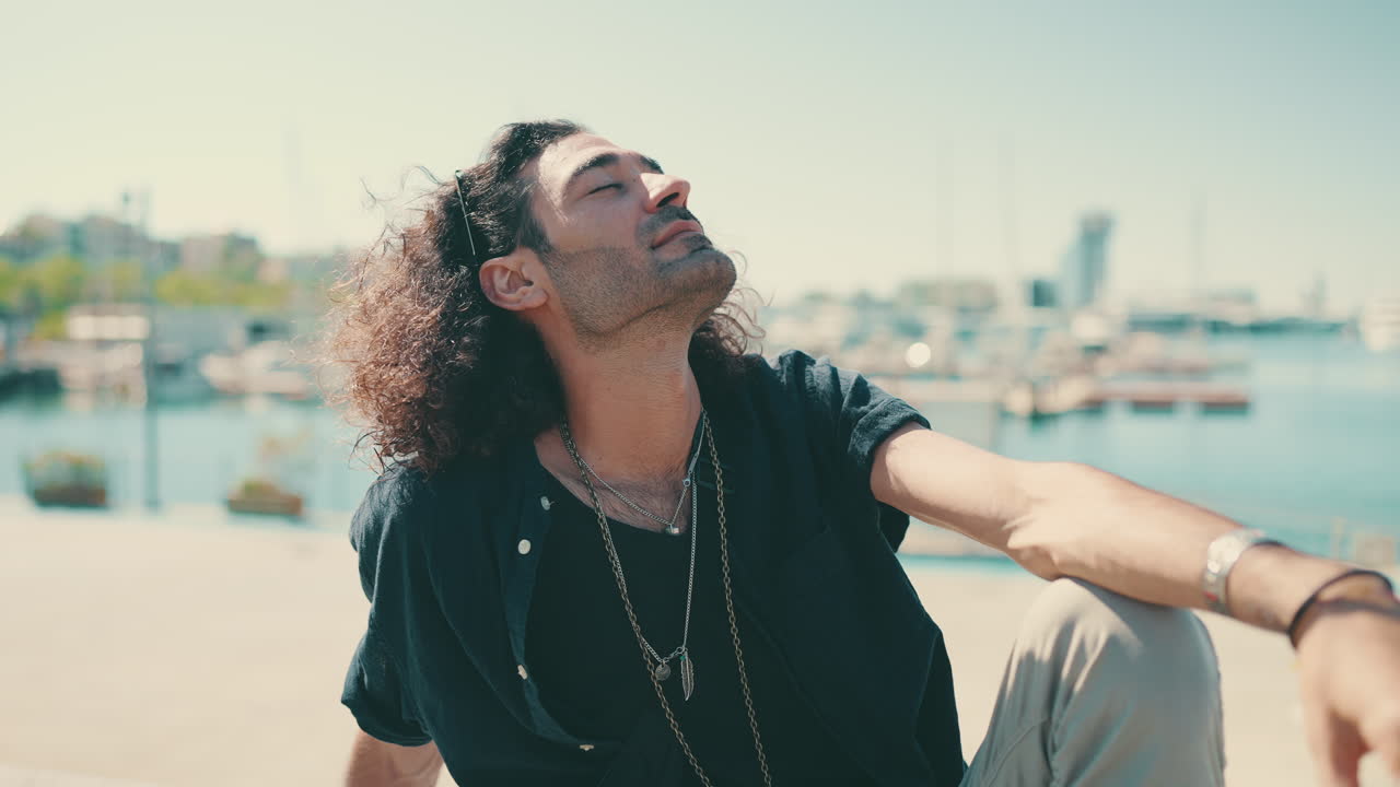 Man with curly hair sitting by the sea