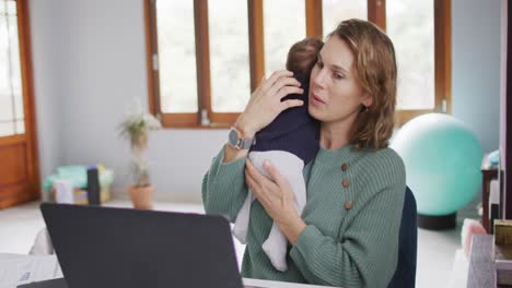 Video-Einer-Kaukasischen-Mutter,-Die-Von-Zu-Hause-Aus-Mit-Ihrem-Neugeborenen-Am-Laptop-Arbeitet