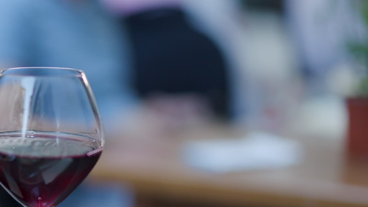 Glass of red wine on table, shallow depth of field, blurred people in background