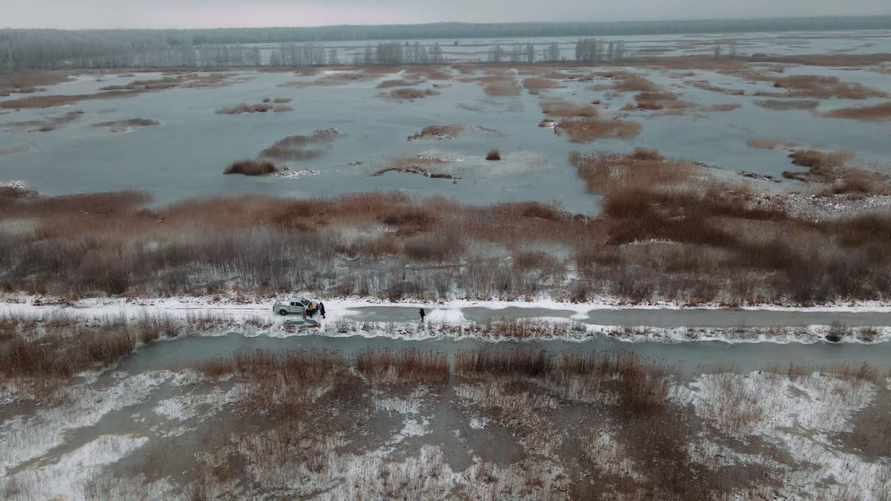 Aerial view of a frozen marshland with patches of ice, brown vegetation, and misty surroundings, creating a cold and desolate winter landscape.