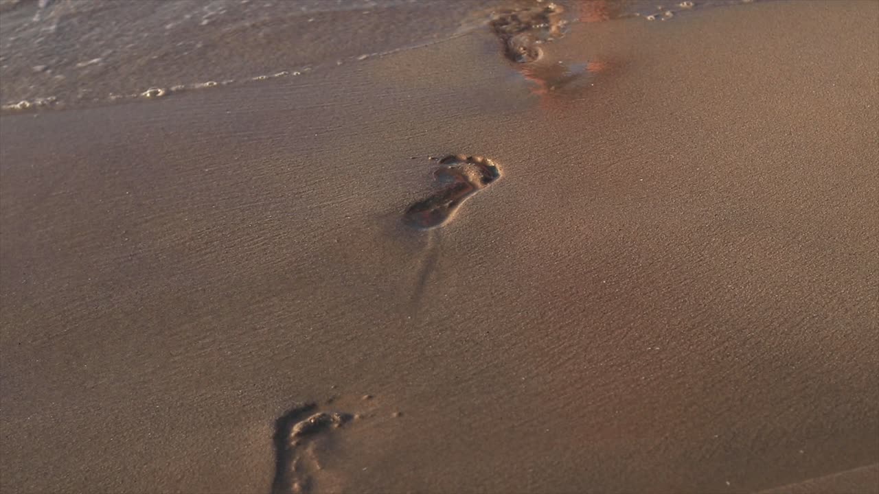 Ragazza che cammina su una spiaggia sabbiosa lasciando impronte dietro di sé.