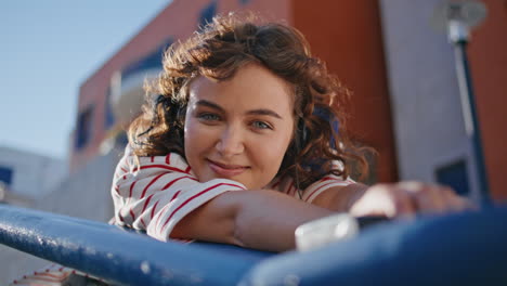 portrait curly woman leaning urban railings looking camera smile. happy girl