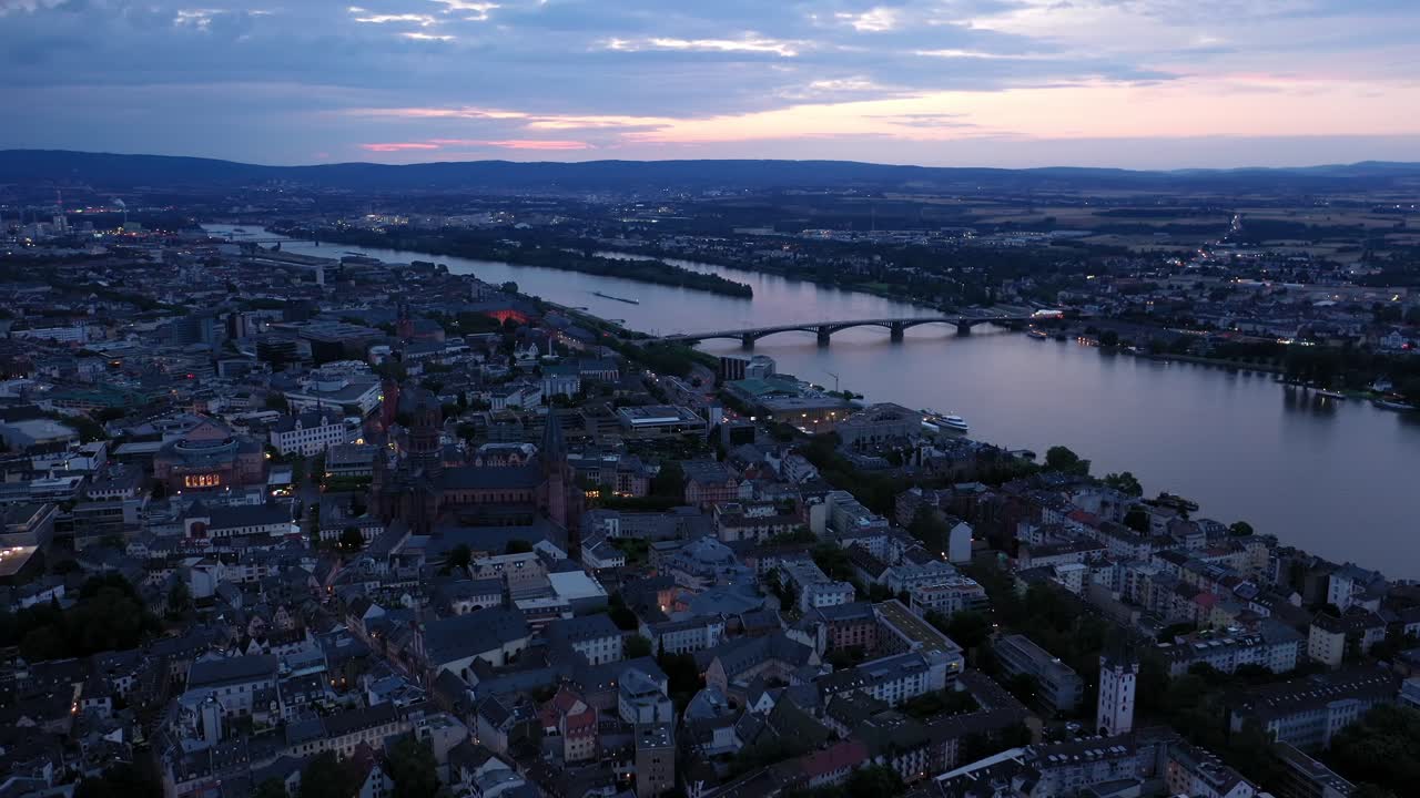 alta toma aérea de drones de maguncia en la hora mágica de la noche dando vueltas alrededor del centro de la ciudad con la catedral y el agua oscura del río rin en el fondo mostrando un cielo colorido