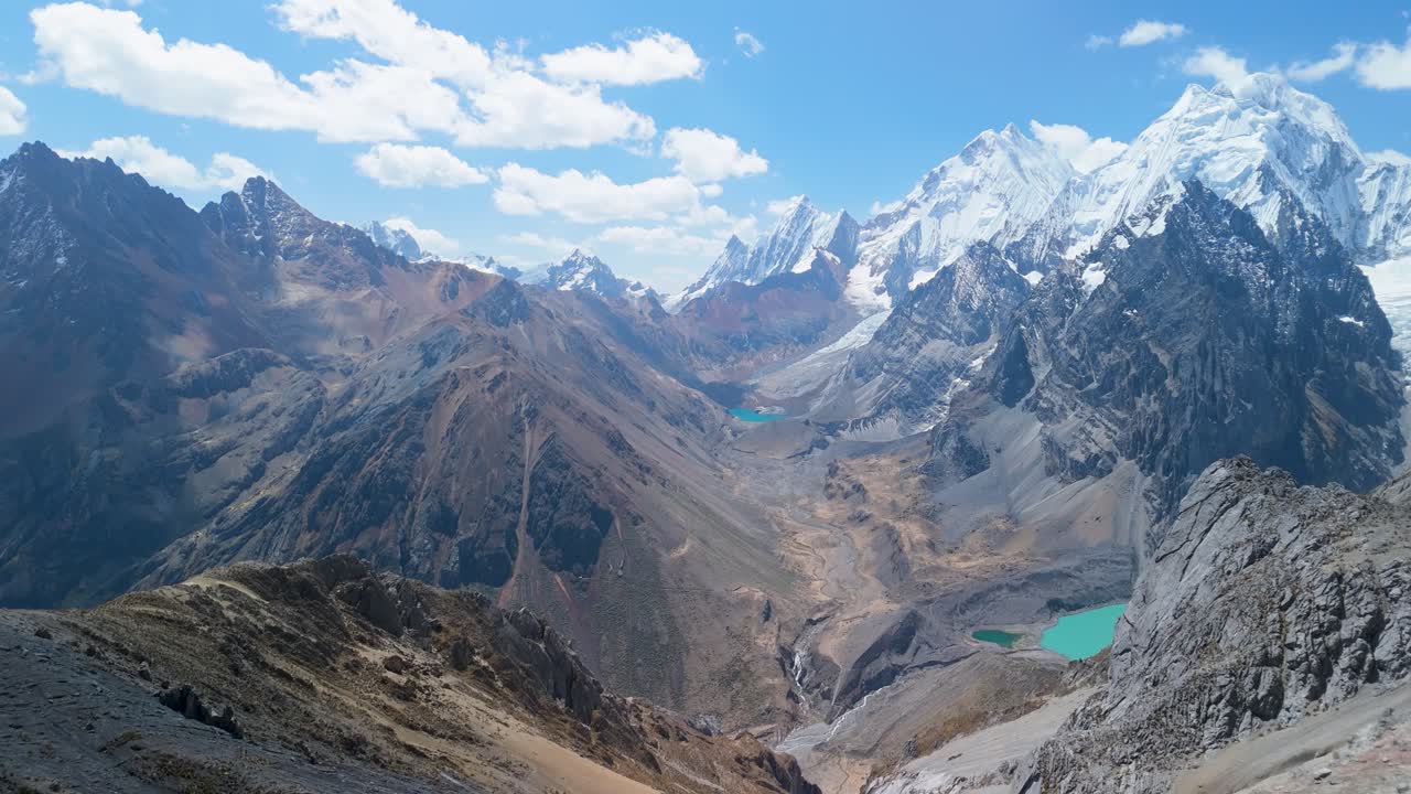 Epic aerial pull back shot from San Antonio Pass reveals panoramic snow-capped peaks, turquoise glacial lakes, and vast wild valleys of the Cordillera Huayhuash in Peru
