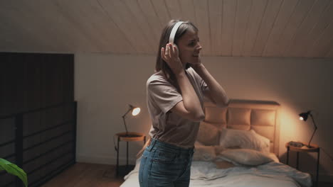 mujer joven con auriculares escuchando música y bailando en el dormitorio por la noche