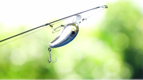 shiny fish-shaped fishing bait with treble hook is attached to a fishing line and attached to a fishing rod