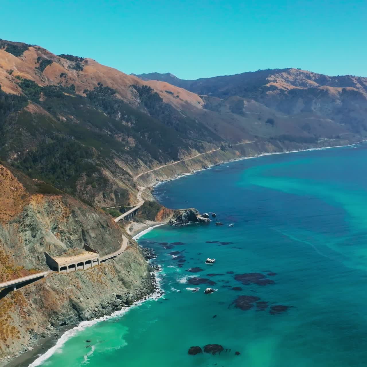 Breath-taking scenery of mountains with some greenery growing on. Turquoise ocean washing the rocky shore. Aerial view