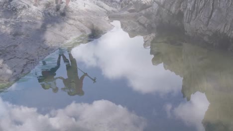 pareja de ancianos caucásicos caminando en rocas reflejadas en el agua, sobre nubes de rápido movimiento