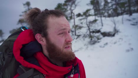 backpacker norwegian guy with beard is hiking during snowstorm in winter mountain