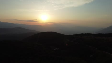 Silhouette-of-mountains-and-bright-sunset-behind,-aerial-view