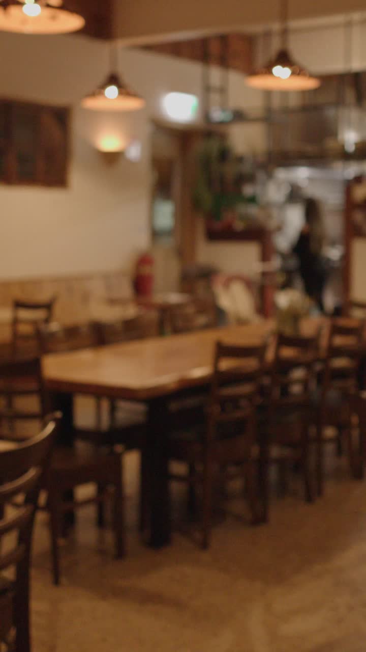Una mano apre la porta di un ristorante, rivelando una sala da pranzo vuota e illuminata calorosamente con mobili in legno rustico