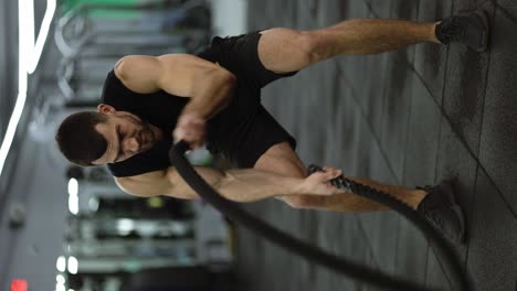 hombre musculoso atractivo trabajando en el gimnasio usando cuerdas de batalla