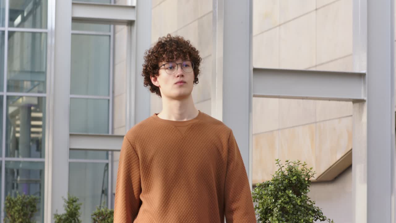 Student betritt das Bild, trägt einen Ordner, geht einen Außengang entlang und begutachtet das Gebäudedesign.