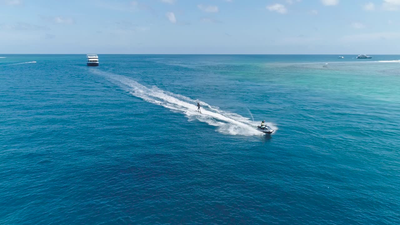 Drone tracking shot Over Man Riding A Jet Ski At Tropical Paradise Exotic Island with blue and turquoise ocean sea view. Adventure Concept for Tourist Attraction at Beach Vacation sport at Summer day